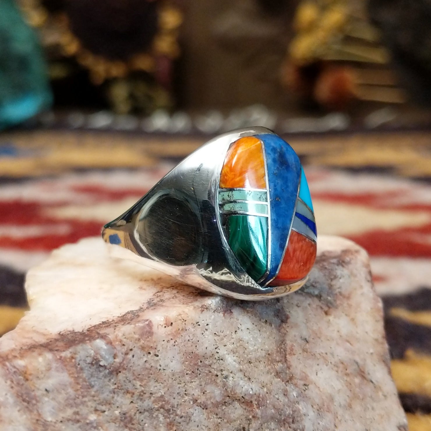 Handcrafted sterling silver multistone inlay ring by Navajo artist Bernadine Joe featuring Denim Lapis, Lapis, red and orange Spiny Oyster Shell, Mother of Pearl, Turquoise, and Malachite arranged in a colorful geometric mosaic design.  Side view.