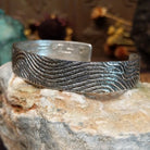 Handcrafted sterling silver cuff bracelet by Dino Garcia featuring a wavy tufa cast design with textured organic detailing in a Southwestern Native American style.  Side view.