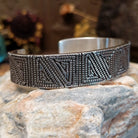 Handcrafted sterling silver cuff bracelet by Elgin Tom featuring geometric pattern detailing in a modern Southwestern Native American design.  Side view.