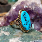 Oval turquoise ring set in a polished 14K yellow gold bezel by Delbert Gordon, featuring natural blue stone with visible matrix patterns and a smooth, minimal gold band design.  Side view.