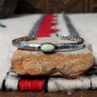 Slender silver cuff by Raymond Coriz featuring a pale green oval Palomino variscite stone centered on a textured, oxidized silver band.