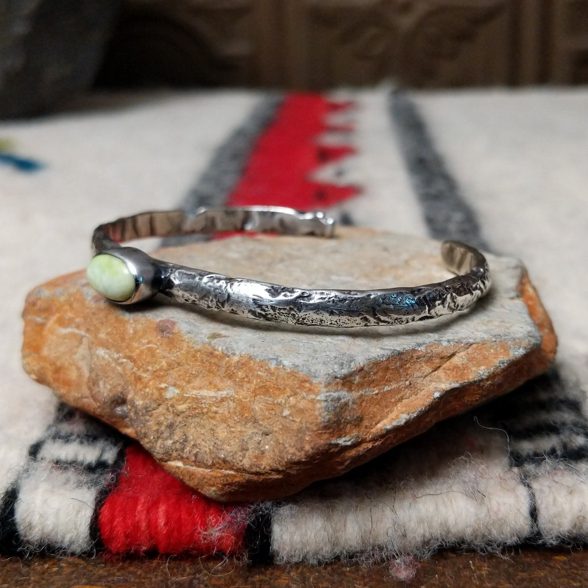 Slender silver cuff by Raymond Coriz featuring a pale green oval Palomino variscite stone centered on a textured, oxidized silver band; side view.