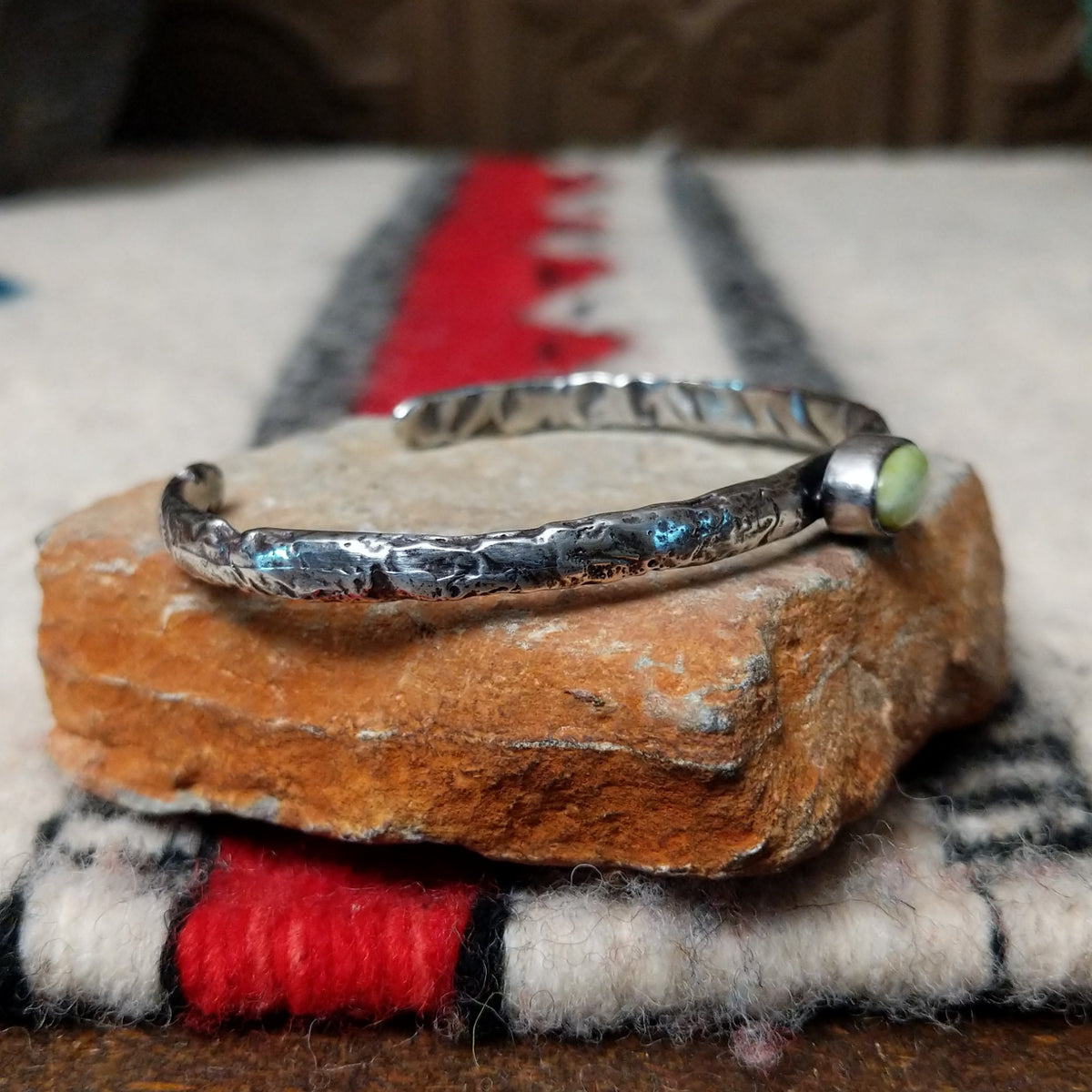 Slender silver cuff by Raymond Coriz featuring a pale green oval Palomino variscite stone centered on a textured, oxidized silver band; side view.