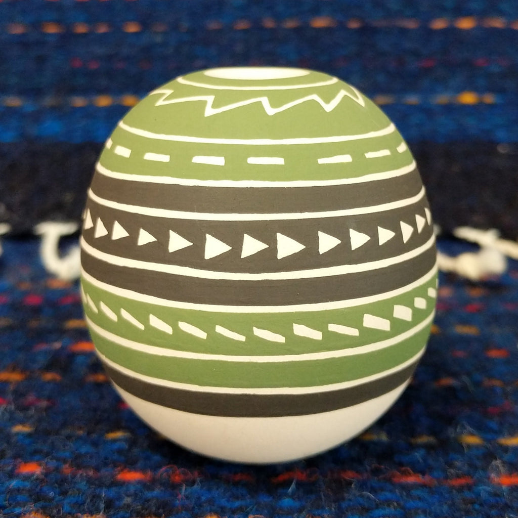 Geometric motifs on the green, brown, and white clay of the piece.