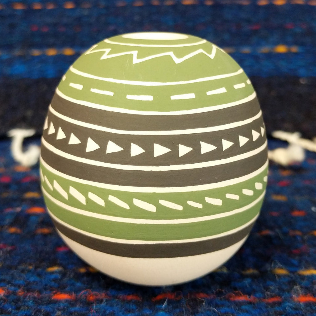 Geometric motifs on the green, brown, and white clay of the piece.