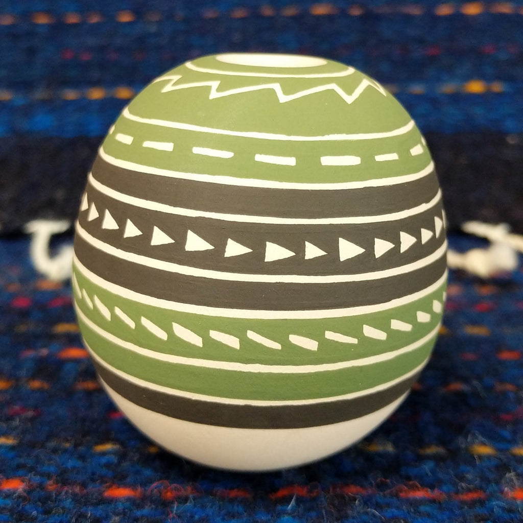 Geometric motifs on the green, brown, and white clay of the piece.