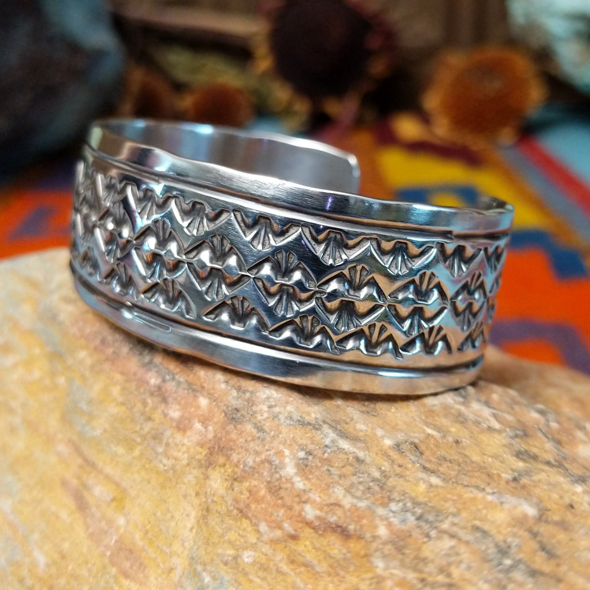 Wide silver cuff by Freddie Maloney with repeating rows of geometric stamped patterns and smooth borders.