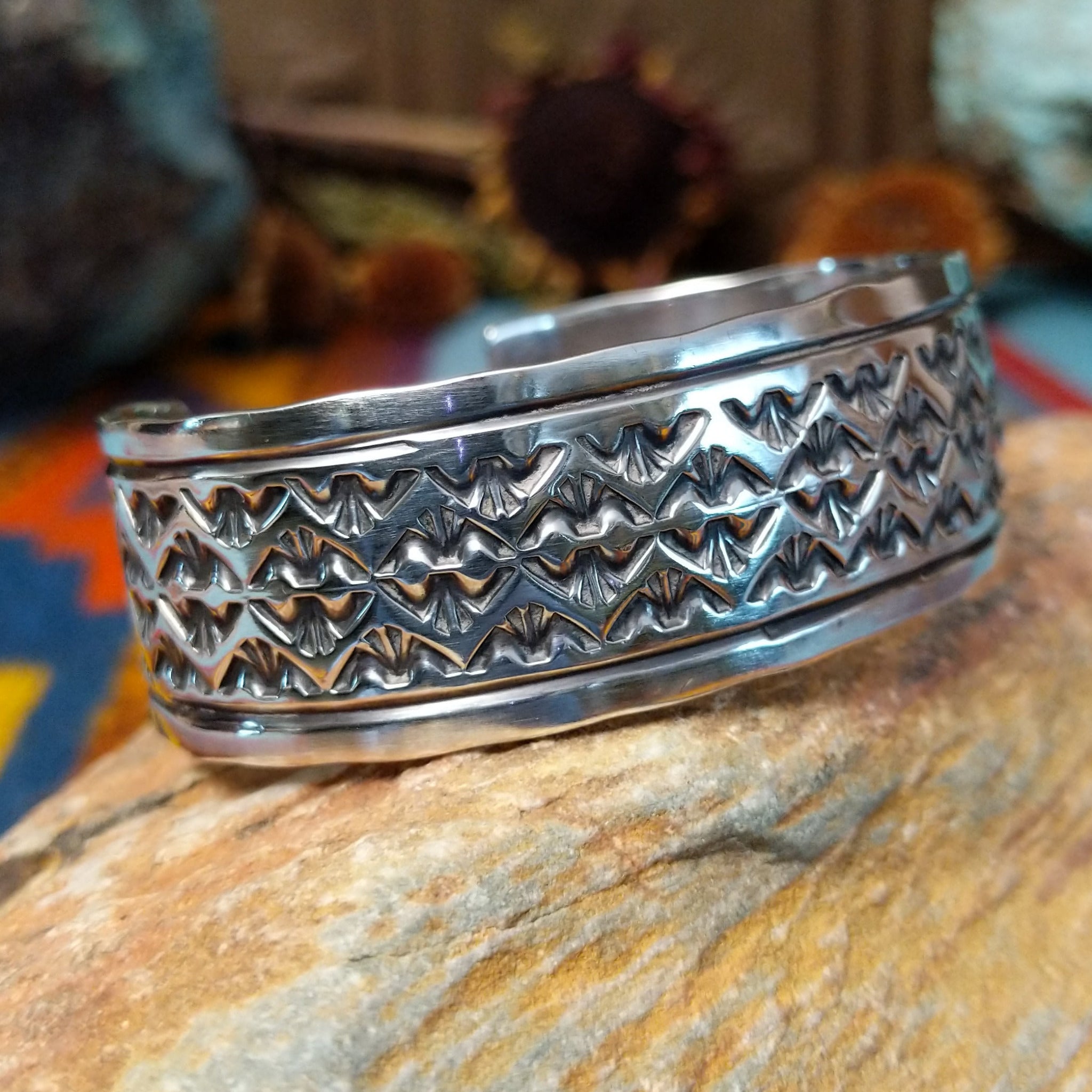 Wide silver cuff by Freddie Maloney with repeating rows of geometric stamped patterns and smooth borders.