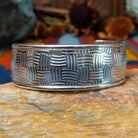 Wide silver cuff by Larry Joe with repeating curved line stampwork arranged in a woven pattern.