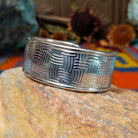 Wide silver cuff by Larry Joe with repeating curved line stampwork arranged in a woven pattern.