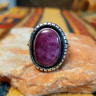 Front view of a silver ring featuring a large oval purple spiny oyster shell cabochon surrounded by a darkened recessed border and segmented silver detailing.