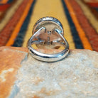 Rear view of a silver ring featuring a large oval purple spiny oyster shell cabochon surrounded by a darkened recessed border and segmented silver detailing. Photo shows the rear of the ring and the polished split-shank band.