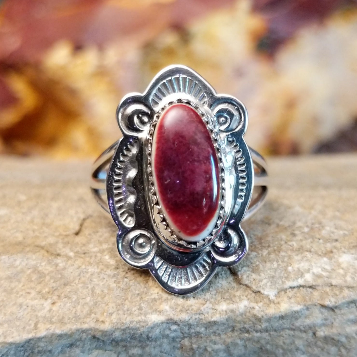 Oval spiny oyster shell set in a notched bezel, framed by ornate, ribbed detailing.