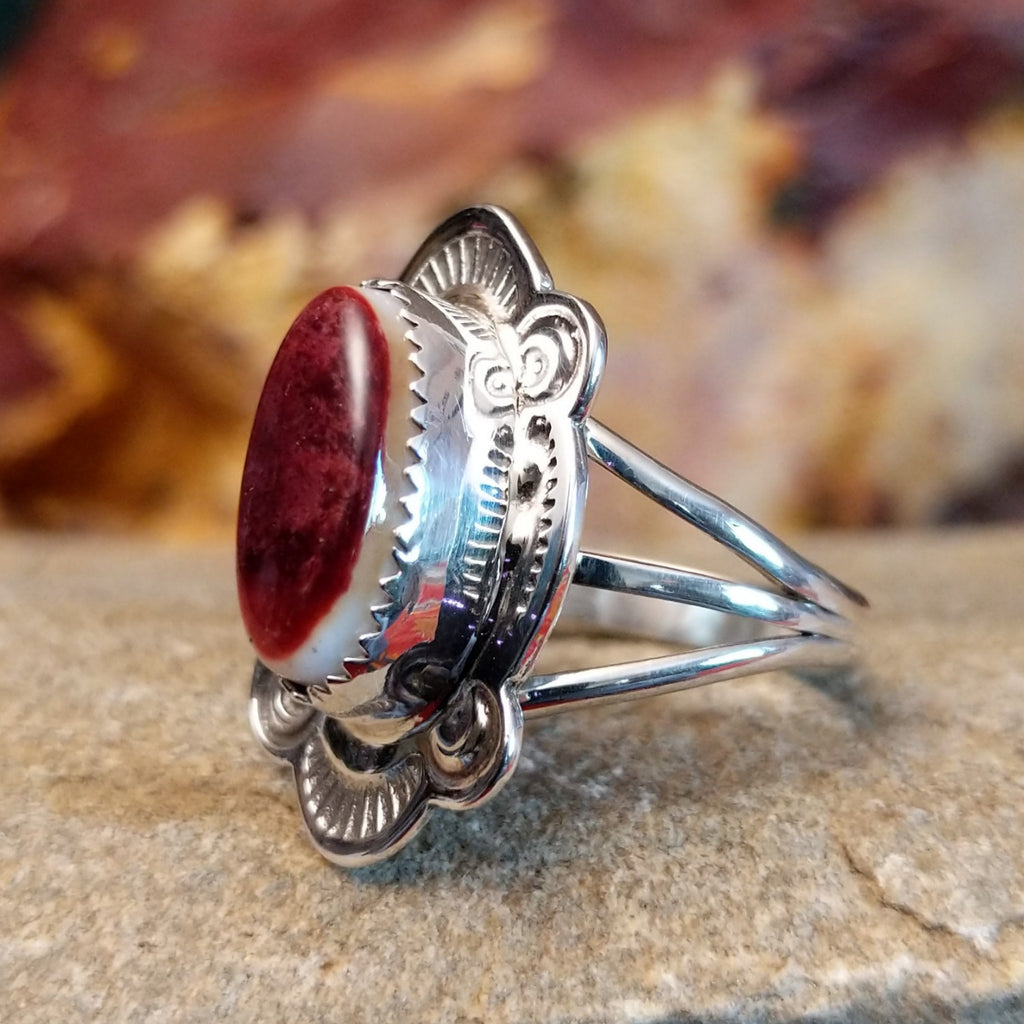 Oval spiny oyster shell set in a notched bezel, framed by ornate, ribbed detailing.