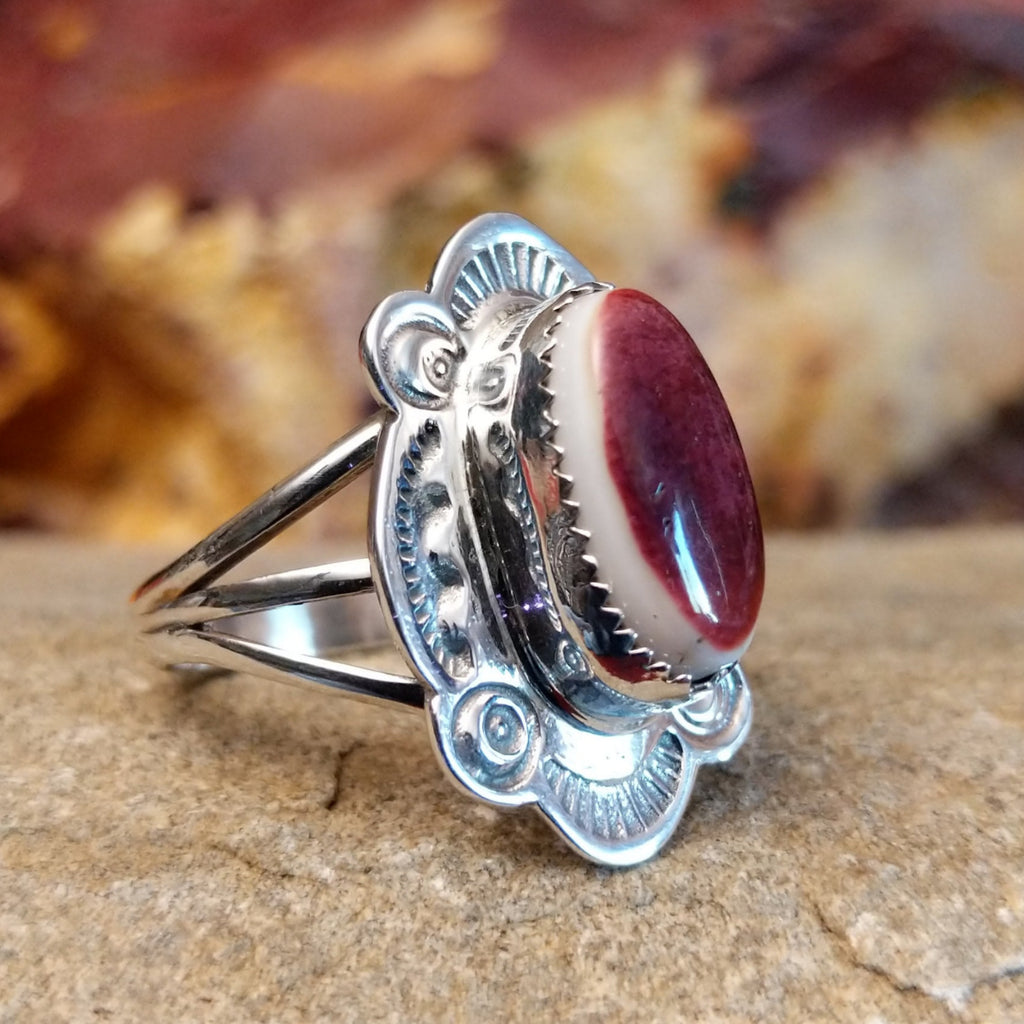 Oval spiny oyster shell set in a notched bezel, framed by ornate, ribbed detailing.