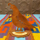 Handcrafted Crooks Design metal quail tabletop sculpture with a curved topknot, cutout wing details, warm rustic finish, and decorative base marked Tombstone, AZ.