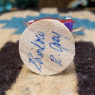 Underside of mini rainbow kachina doll showing handwritten signature and label on wood base.