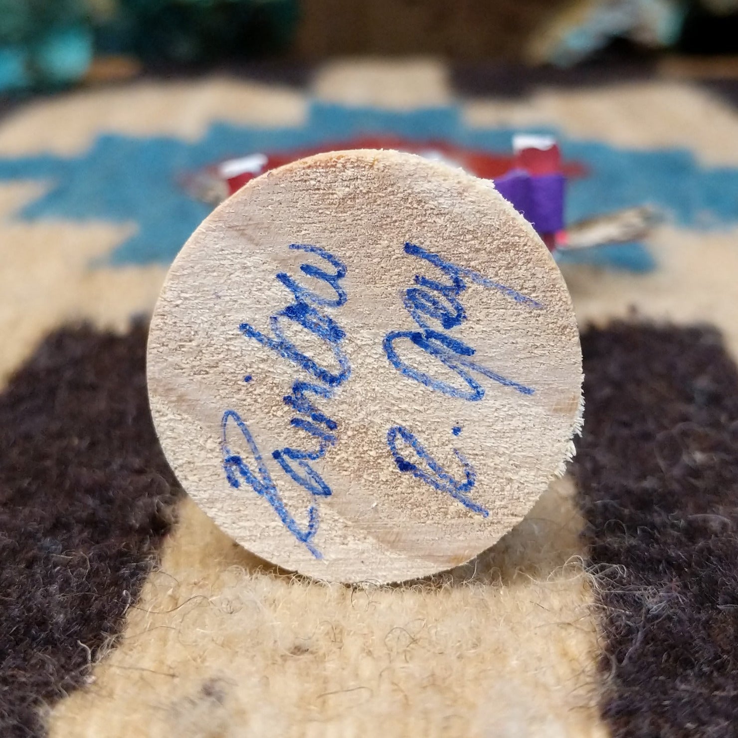 Underside of mini rainbow kachina doll showing handwritten signature and label on wood base.