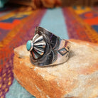 Raised #8 Turquoise Ring by Chris Billie featuring an oval turquoise stone centered within a raised silver flower, surrounded by detailed stamped and oxidized silverwork on a wide band; side view.