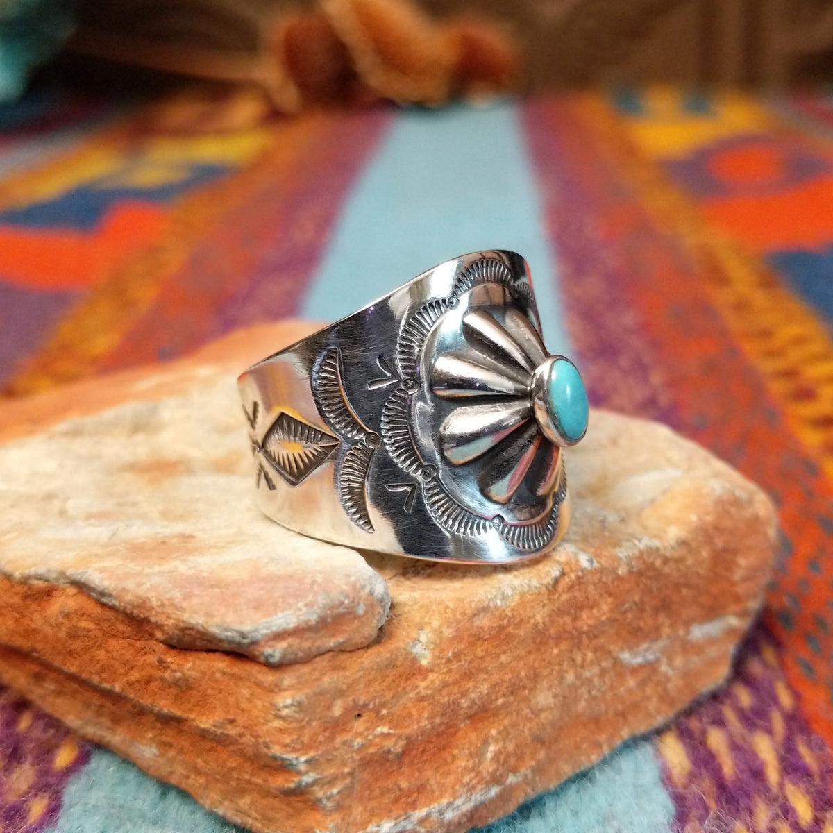 Raised #8 Turquoise Ring by Chris Billie featuring an oval turquoise stone centered within a raised silver flower, surrounded by detailed stamped and oxidized silverwork on a wide band; side view.