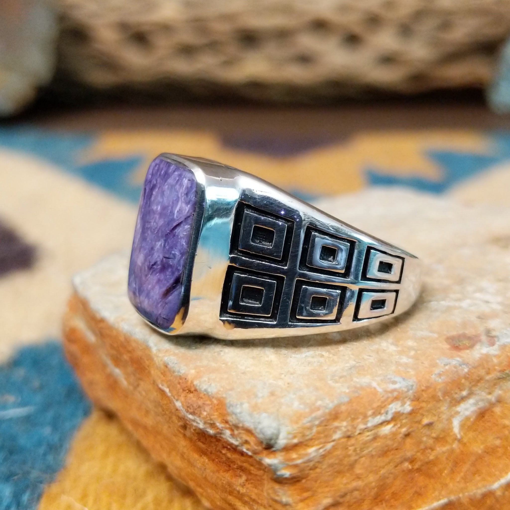 Handcrafted Navajo sterling silver ring by Terry Wood featuring a raised rectangular charoite cabochon with natural purple swirling patterns, set in a polished silver bezel with geometric detailing on the band; side view.