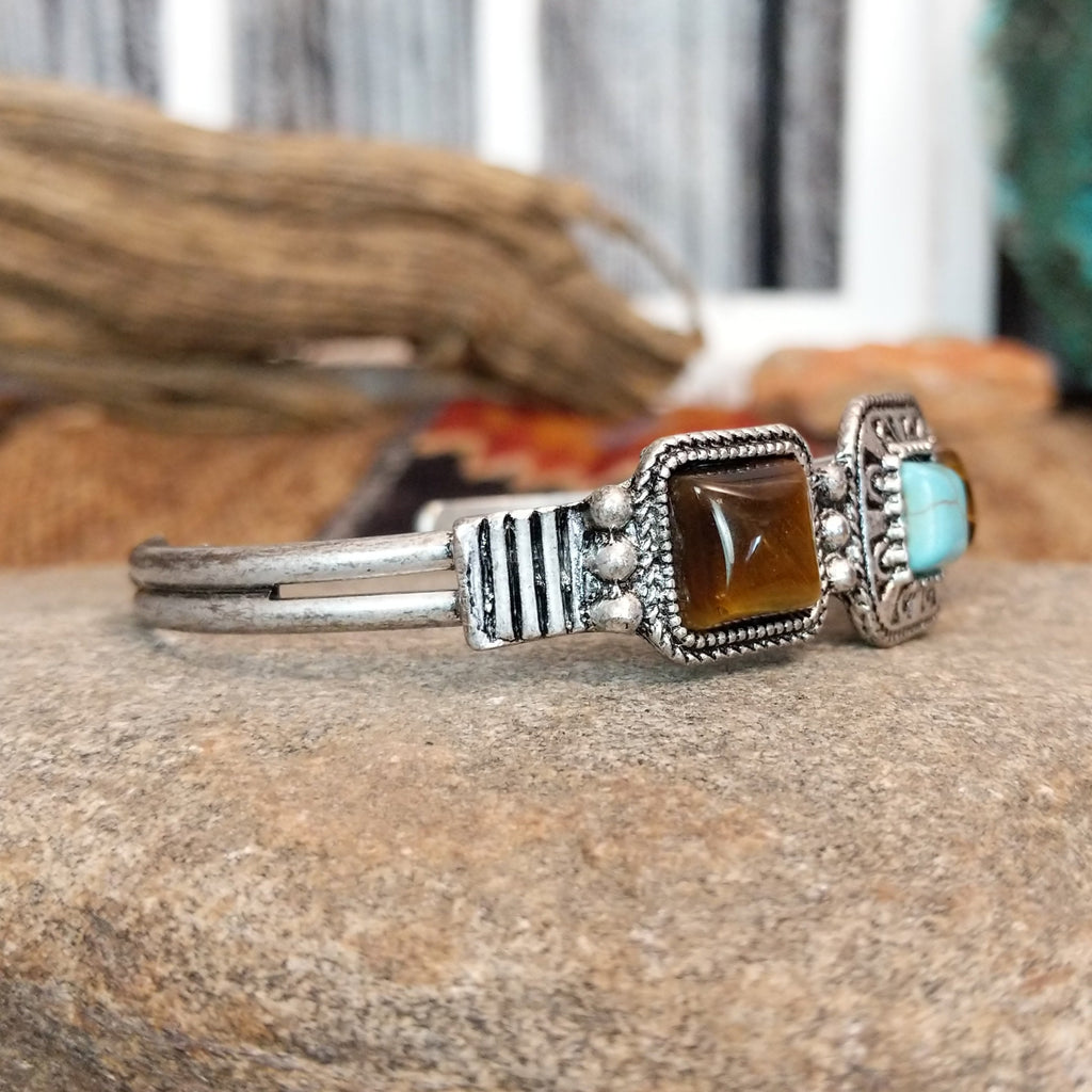 A nickel-free metal cuff bracelet with a central turquoise stone flanked by two tiger’s eye stones.