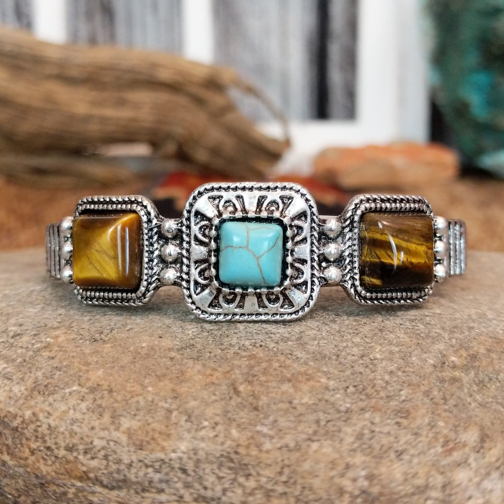 A nickel-free metal cuff bracelet with a central turquoise stone flanked by two tiger’s eye stones.