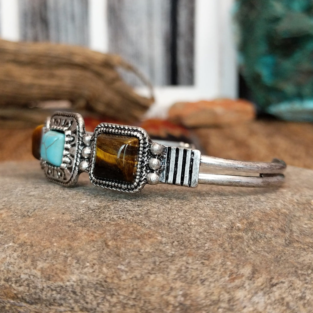 A nickel-free metal cuff bracelet with a central turquoise stone flanked by two tiger’s eye stones.