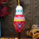 This charming Red Bulb Wool Ornament by Ganz features a bright red wool body with white embroidered geometric designs, blue and yellow floral accents, lavender and yellow bands, a fluffy white top with blue stitching, and a gold hanging cord.