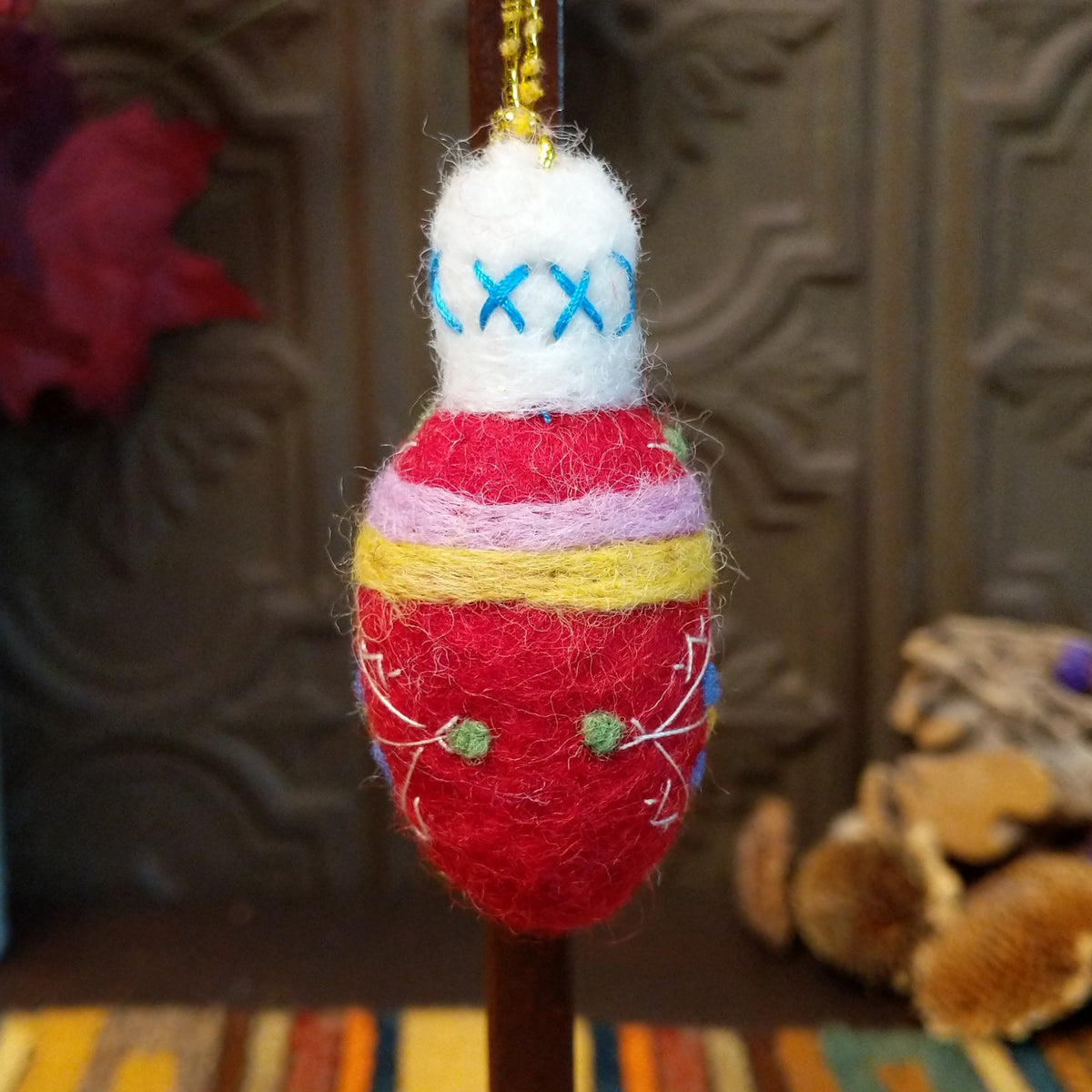 This charming Red Bulb Wool Ornament by Ganz features a bright red wool body with white embroidered geometric designs, blue and yellow floral accents, lavender and yellow bands, a fluffy white top with blue stitching, and a gold hanging cord.
