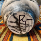 Close-up of the underside of Roger Calhoun's horsehair pottery, showing the artist's hand-painted initials on the unglazed base.