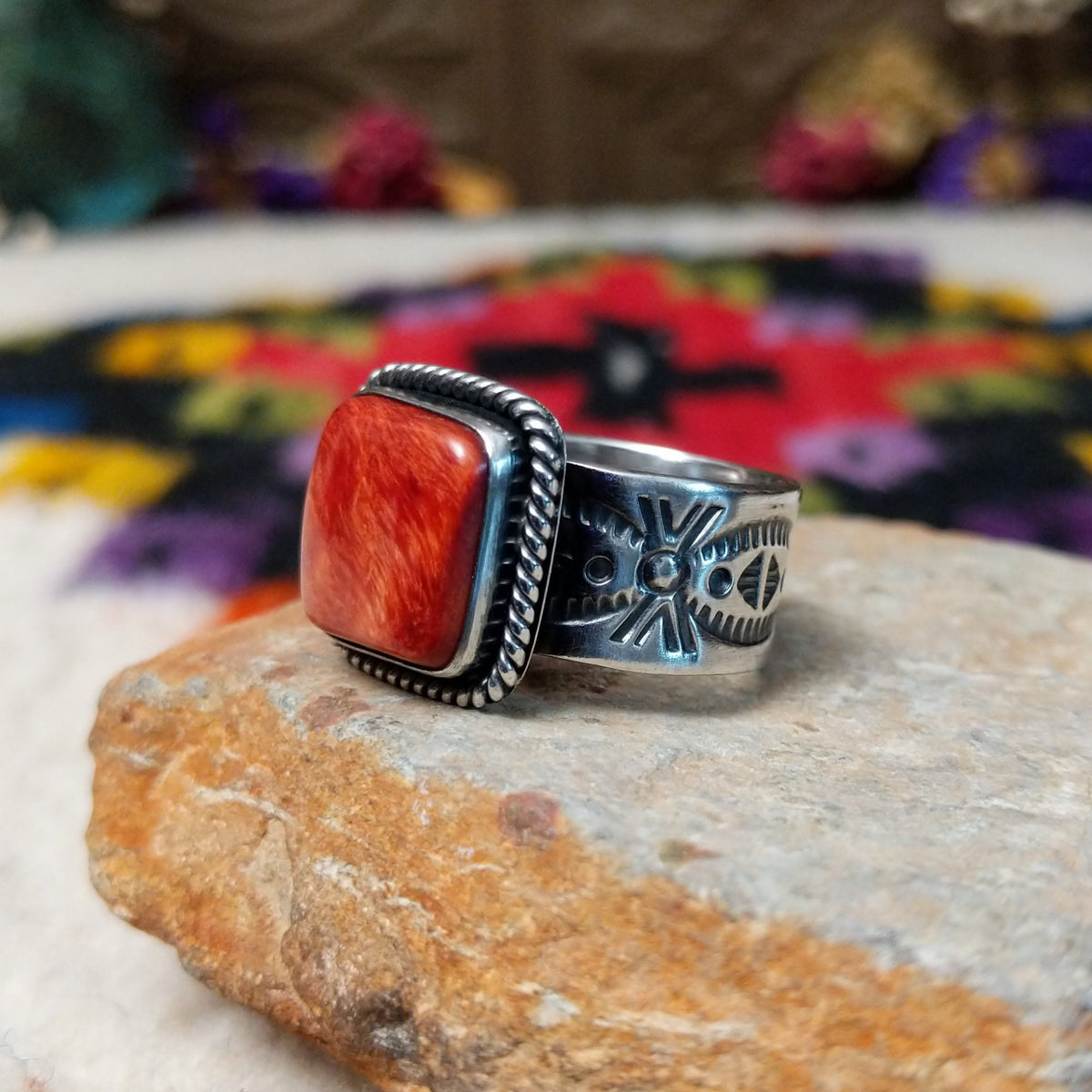 Red Spiny Oyster Shell Ring by Raymond Coriz with a square red-orange cabochon, twisted rope-style sterling silver border, and stamped silver band; side view.