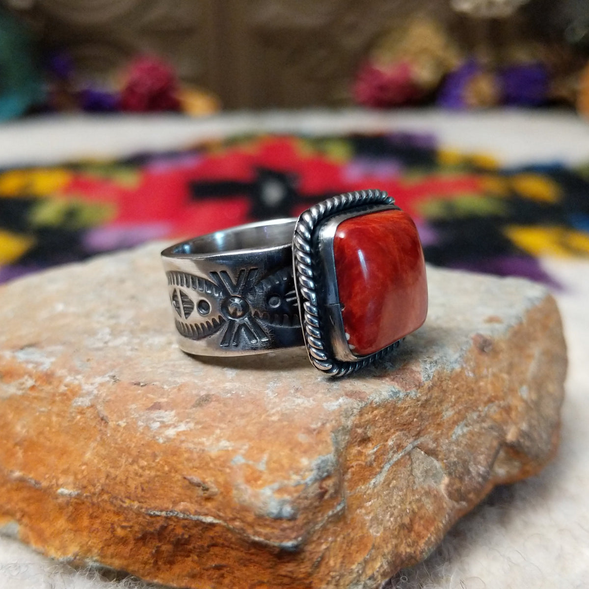 Red Spiny Oyster Shell Ring by Raymond Coriz with a square red-orange cabochon, twisted rope-style sterling silver border, and stamped silver band; side view.