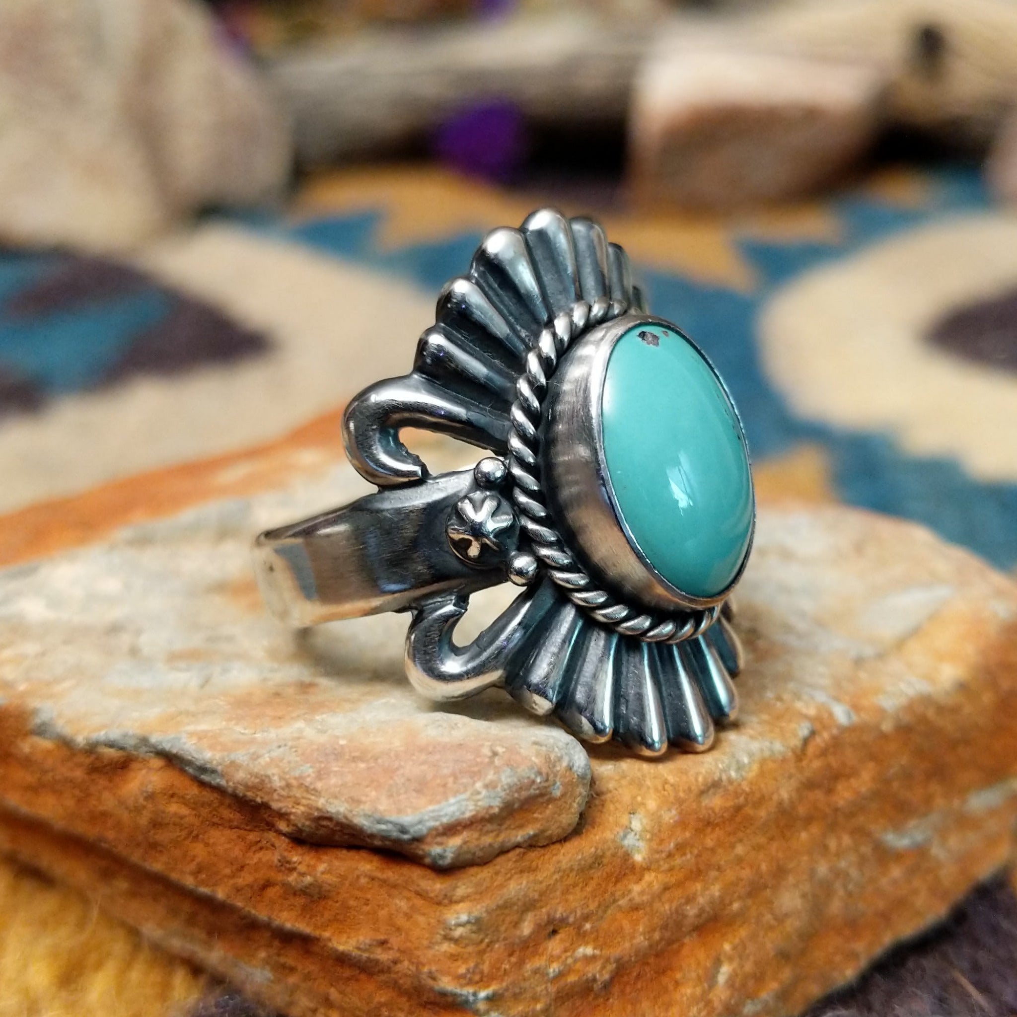 Sterling silver turquoise ring by Raymond Coriz featuring an oval turquoise cabochon, twisted rope bezel, concho-inspired fan design, and intricate Southwestern silverwork; side view.