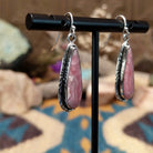 Handcrafted sterling silver teardrop earrings by John King featuring natural rhodochrosite with soft pink and white banding in hand-stamped sterling silver settings on French hooks; side view.