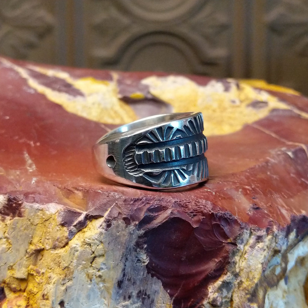 Silver ring with intricate design on a textured silver surface