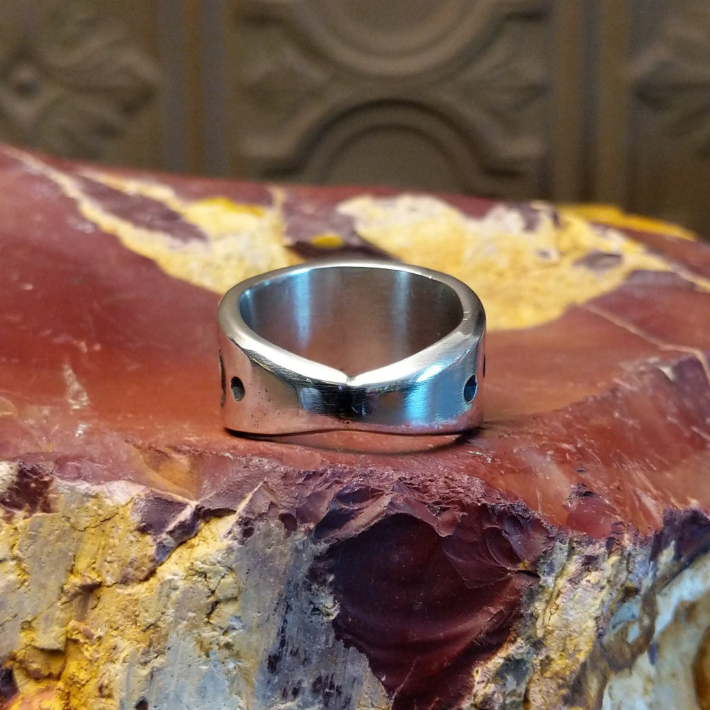 Silver ring with intricate design on a textured silver surface