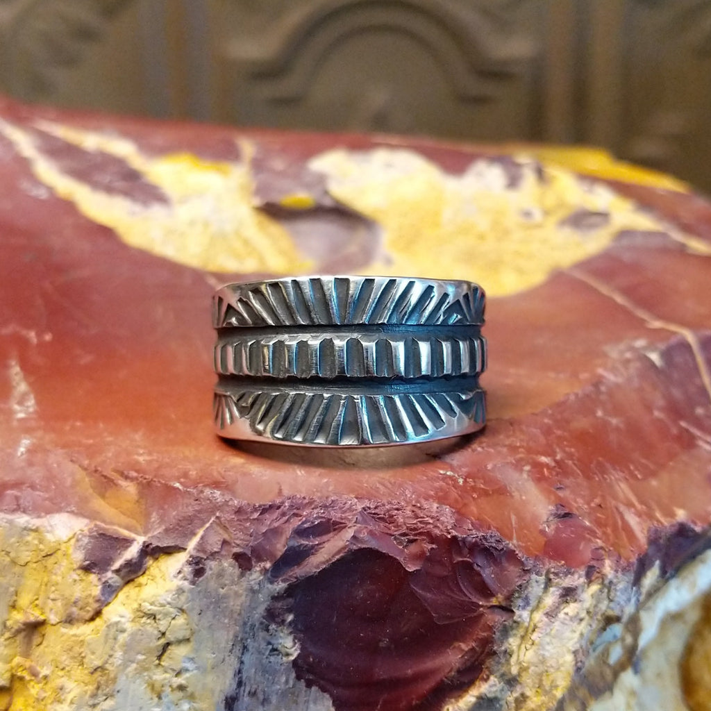 Silver ring with intricate design on a textured silver surface
