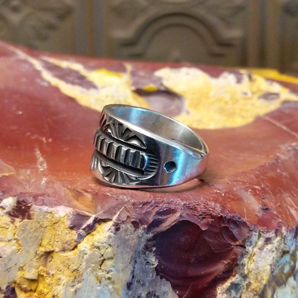 Silver ring with intricate design on a textured silver surface