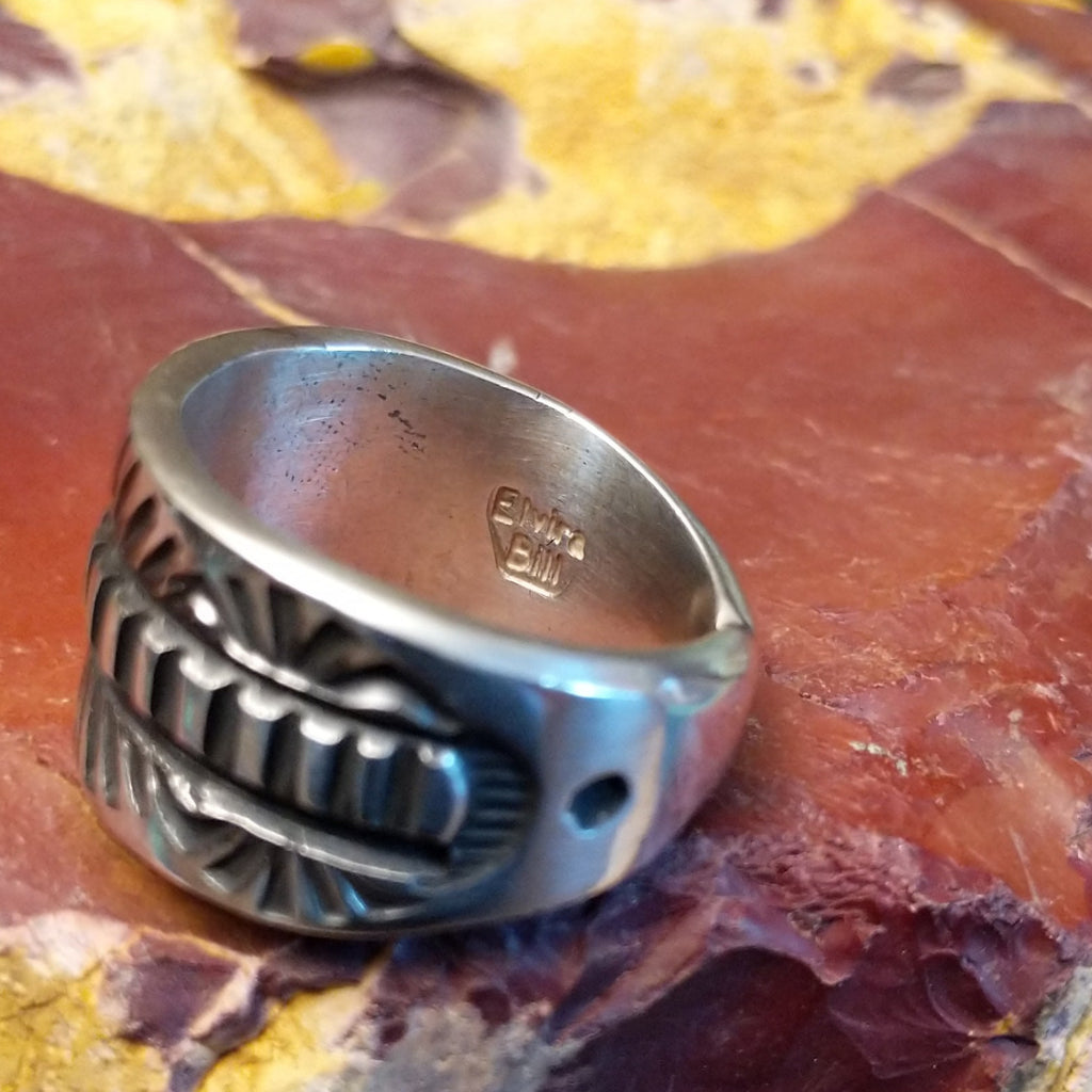 Silver ring with intricate design on a textured silver surface