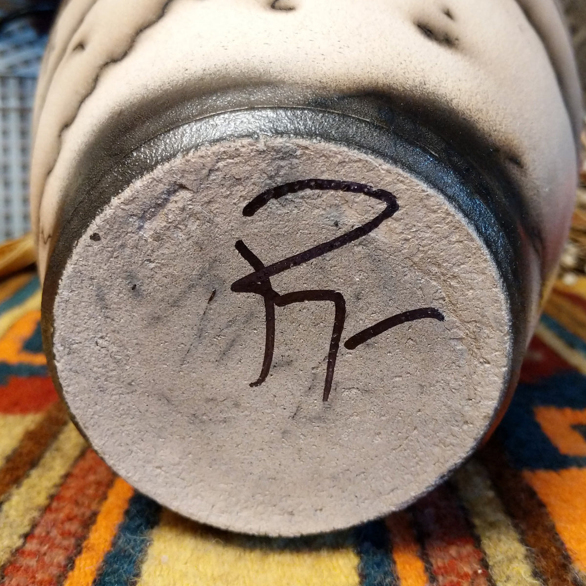 Close-up of the underside of Roger Calhoun's horsehair pottery, showing the artist's hand-painted initials on the unglazed base.