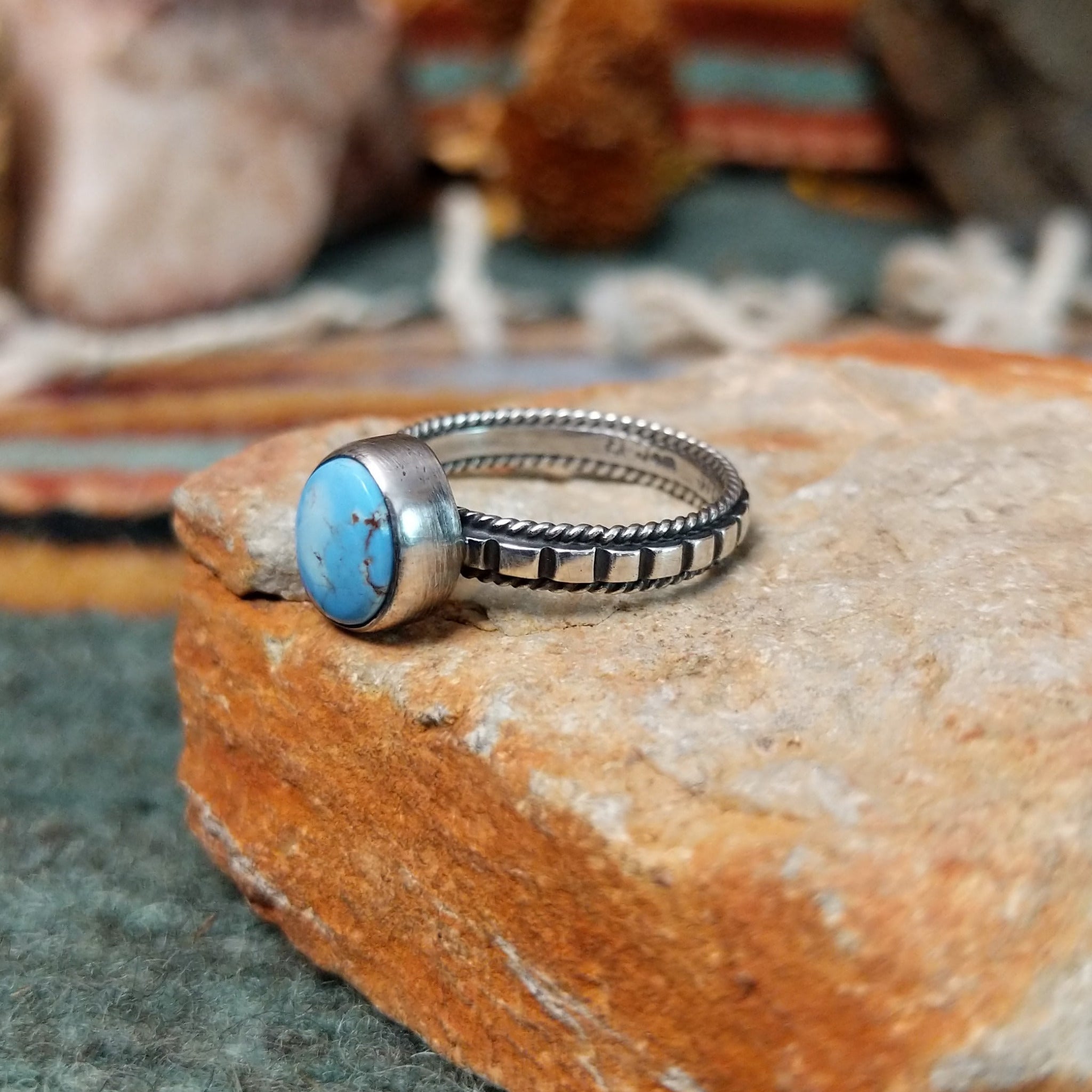 Sterling silver ring by Elgin Tom featuring an oval Golden Hills turquoise stone with natural matrix and a detailed silver band; side view.