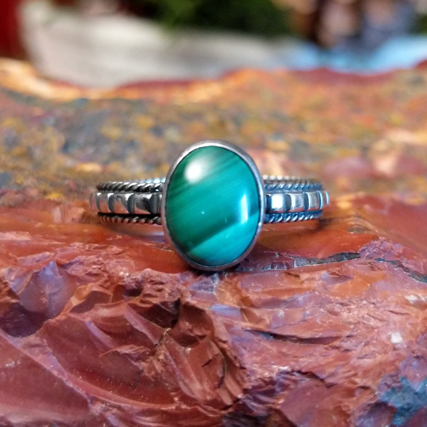 Sterling silver ring with patterned band, twisted rope accents, and malachite set in the round bezel.