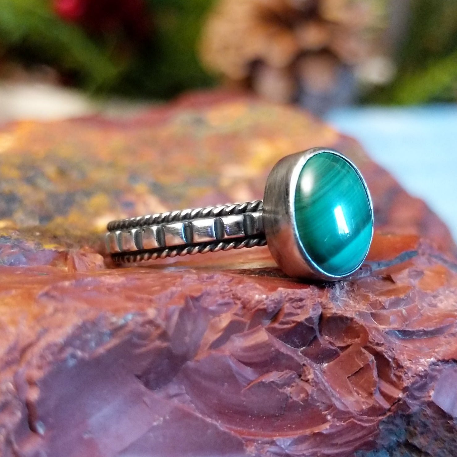 Sterling silver ring with patterned band, twisted rope accents, and malachite set in the round bezel.