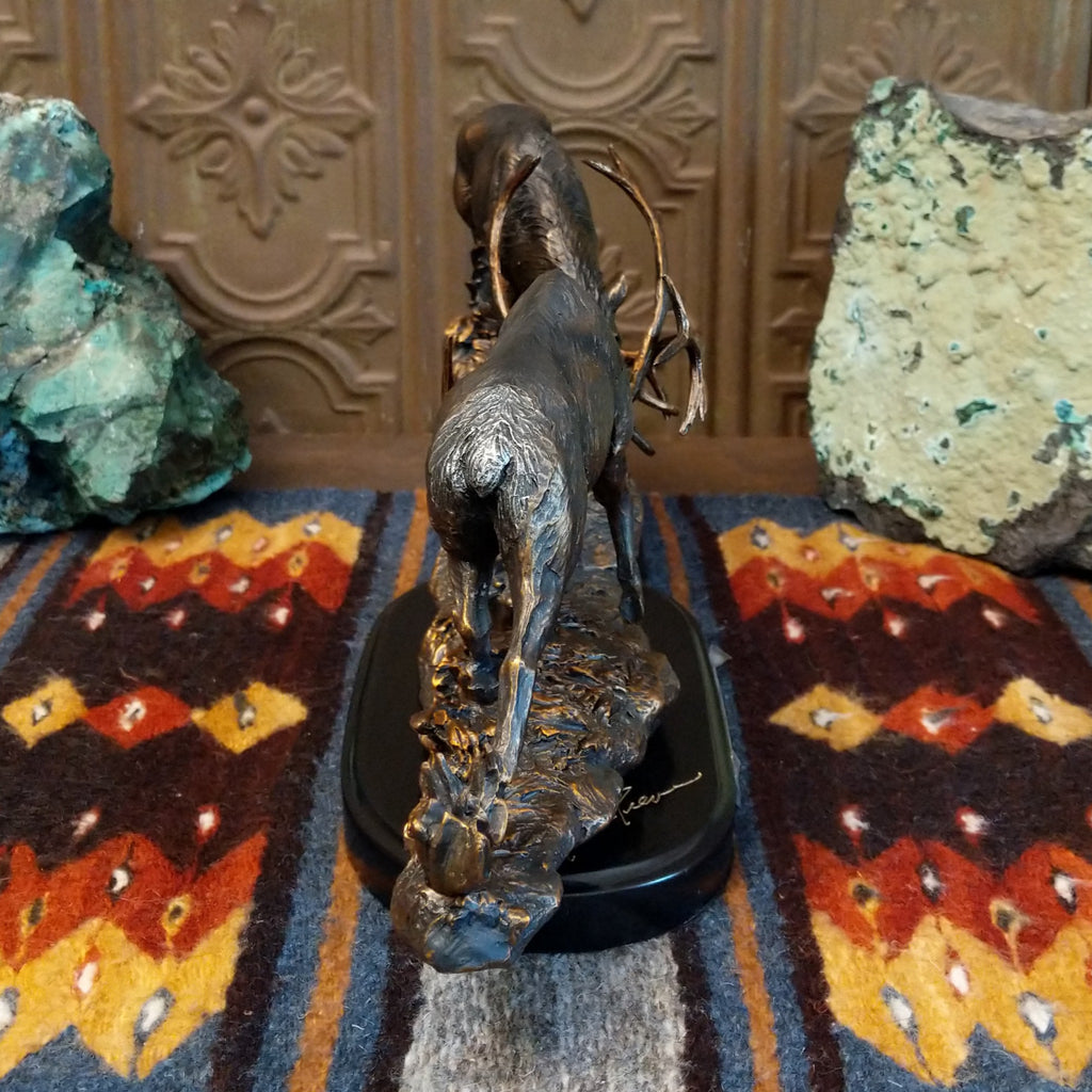 Sculpture showing two bronze stags with antlers locked in combat on a textured base.