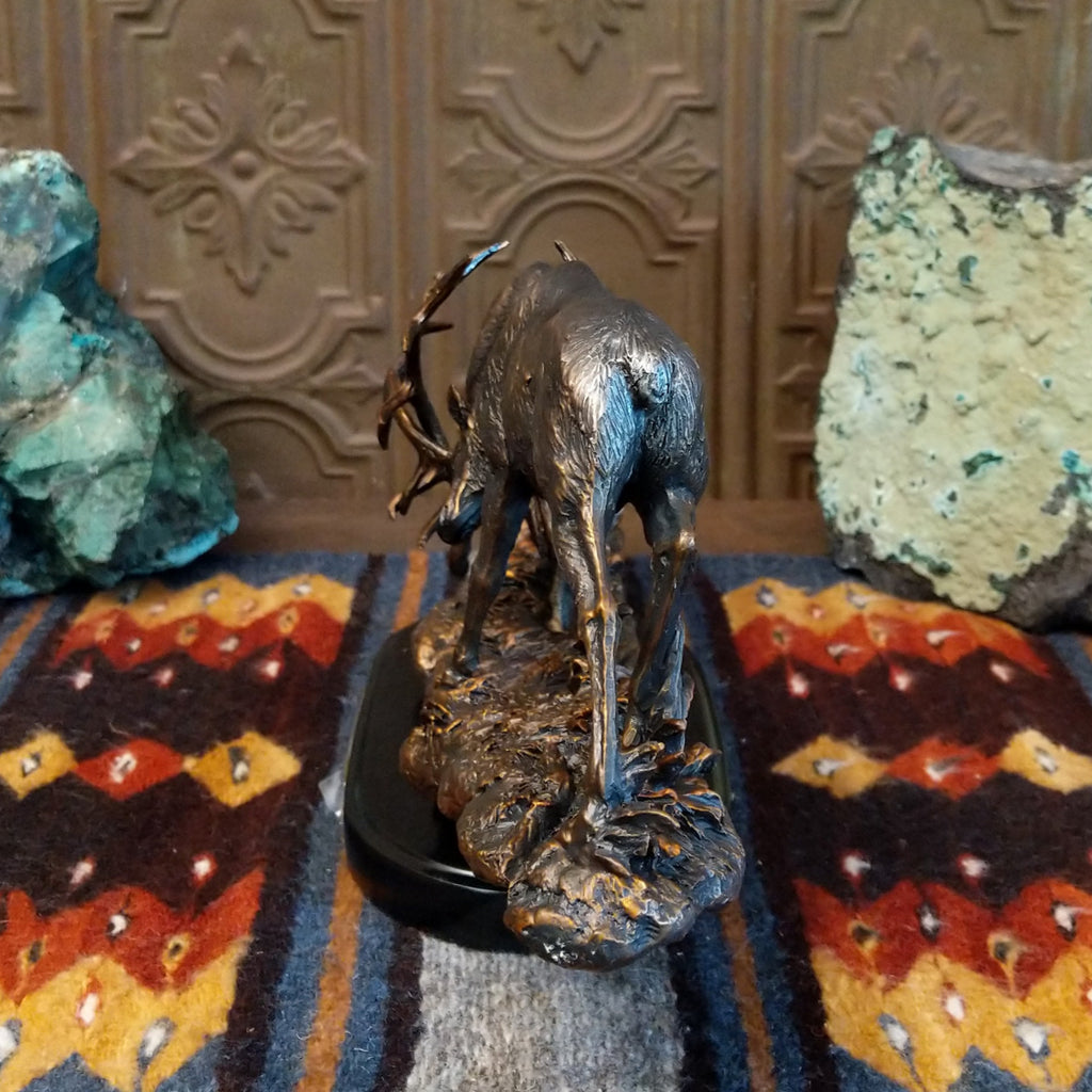 Sculpture showing two bronze stags with antlers locked in combat on a textured base.