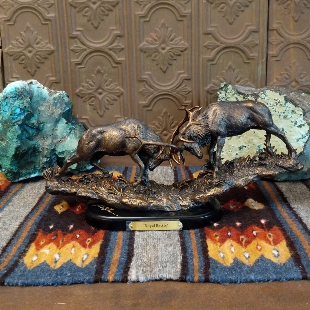 Sculpture showing two bronze stags with antlers locked in combat on a textured base.
