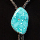 A turquoise stone bolo tie with a braided black cord, displayed on a black velvet jewelry bust.