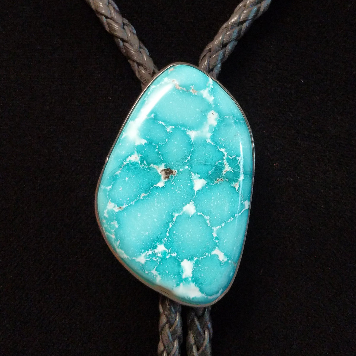 A turquoise stone bolo tie with a braided black cord, displayed on a black velvet jewelry bust.