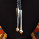 A close-up of a silver engraved details and spherical bead ends, hanging against a black display bust.